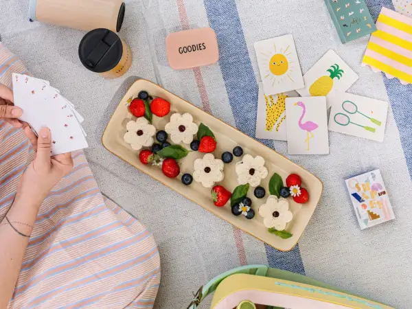 Picnic per bambini con panini a forma di fiore, fragole, mirtilli e carte da gioco colorate.