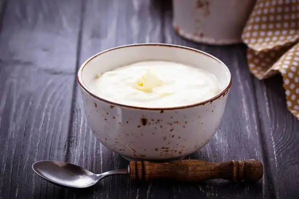 Una ciotola di semolino dosi per 1 persona con latte, guarnita con un pezzetto di burro. Un cucchiaio di legno è appoggiato accanto.