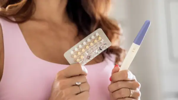 Donna tiene in mano un blister di pillole anticoncezionali e un test di gravidanza positivo. Si interroga su come rimanere incinta con la pillola e sui sintomi.
