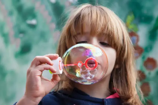 Bambina soffia bolle di sapone iridescenti. Una ricetta veloce per un momento di gioia.