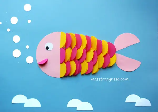 Pesciolino colorato creato con lavoretti per bambini in estate. Bollicine e onde di carta completano la scena marina.