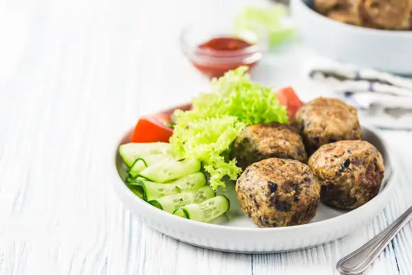 Polpette lenticchie e patate dorate, servite con insalata fresca, pomodoro e cetrioli a spirale. Un piatto gustoso e salutare.