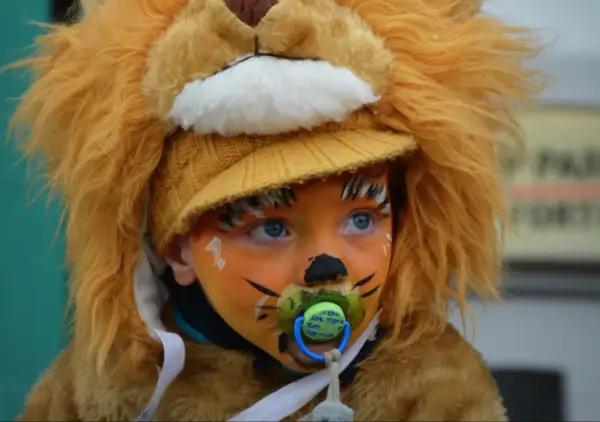 Bambino con trucco carnevale facile da leone, con ciuccio e cappello giallo.