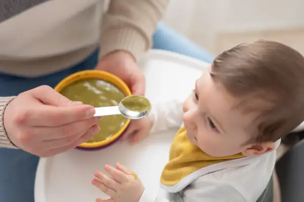 Bambino curioso assaggia la sua prima pappa svezzamento, con un cucchiaino pieno di verdure.