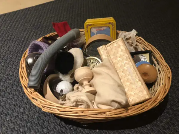 Un cestino dei tesori pieno di oggetti curiosi: un tubo grigio, una pallina da golf, un piccolo specchio, una scatola gialla e altri elementi da esplorare.