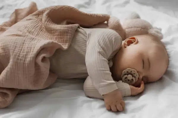 Dolce neonato di 3 mesi dorme sereno, avvolto in una copertina color pesca, con un ciuccio in bocca.