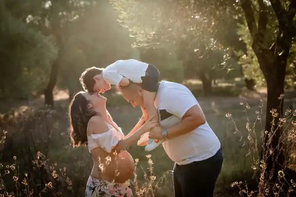 Una bellissima giornata della famiglia, con un bimbo sulle spalle del papà che bacia la mamma in dolce attesa, immersi nella luce dorata del tramonto.