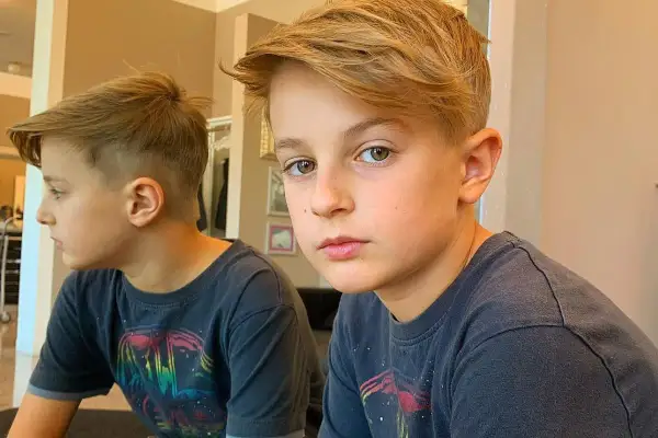 Un bambino di 10 anni con un taglio capelli moderno, capelli biondi sfilati e sfumati ai lati.